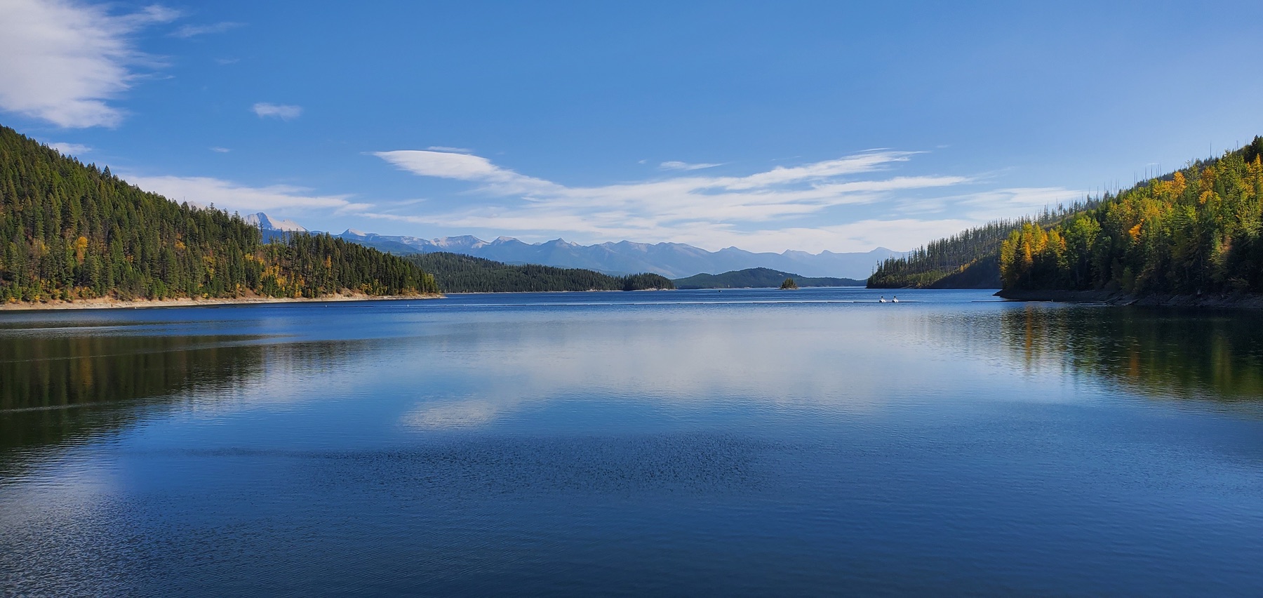 Forested shoreline and mountains reflected in a calm Montana lake